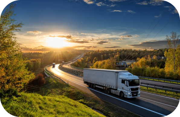 White freight truck driving on a scenic highway at sunset, surrounded by trees and a beautiful landscape