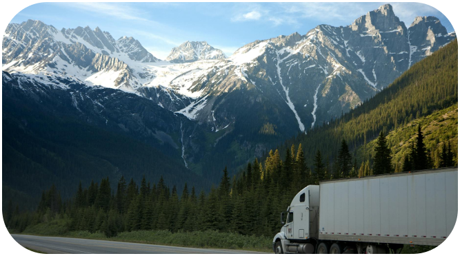 White freight truck driving along a highway with snow-capped mountains in the background
