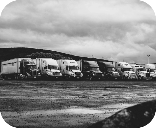 Row of parked freight trucks in a lot under a cloudy sky, black-and-white photo