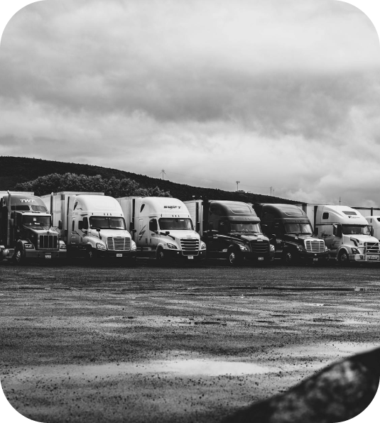 Row of parked freight trucks in a lot under a cloudy sky, black-and-white photo